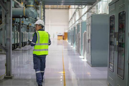 Power station staff working in industrial facility wearing safety helmet and reflective vest inspecting electrical equipment in clean environment