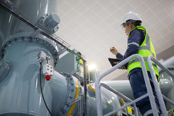Power station staff inspect industrial equipment carefully with safety gear and clipboard ensuring...