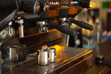 Barista. The pitchers are located under the illuminated coffee machine groups. The background is blurred and has neutral colors