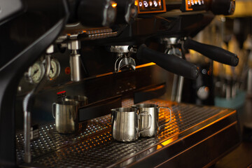 Barista. The pitchers are located under the illuminated coffee machine groups. The background is blurred and has neutral colors