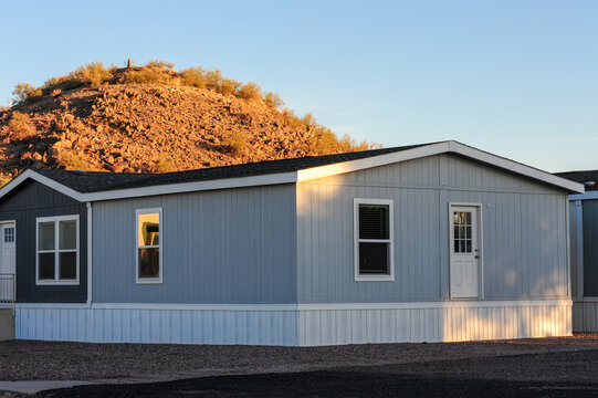 A manufactured home with vinyl siding and skirting is installed on a prepared lot, representing modular housing in a residential development setting