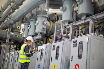 Power station engineer working on electrical equipment in industrial facility with safety helmet and reflective vest showing focus and professionalism