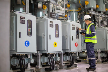 Power circuit breaker inspection at substation with technician wearing safety helmet and reflective vest checking electrical control panel using digital tablet