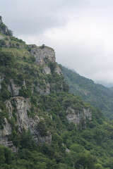 Naklejka premium Rugged mountain peaks meet winding road in Asón, Cantabria - Breathtaking Cantabrian valley with lush green forests, rugged mountains, and serene atmosphere, set amidst a natural.
