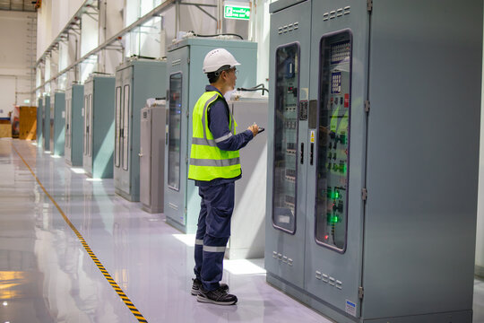 Engineer inspects local control cabinet in substation with focus and safety gear, ensuring proper operation and maintenance of electrical systems in industrial environment