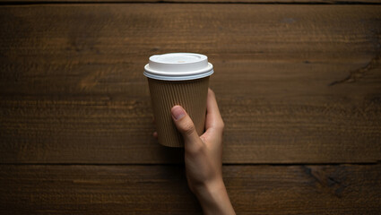 Hand holding a disposable coffee cup with a lid on a wooden background