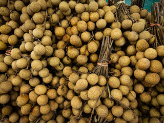 A top-down, detailed shot of numerous longan fruit bunches, their rough, light brown skin and stems visible in a bountiful and rustic display, likely at a market stall.