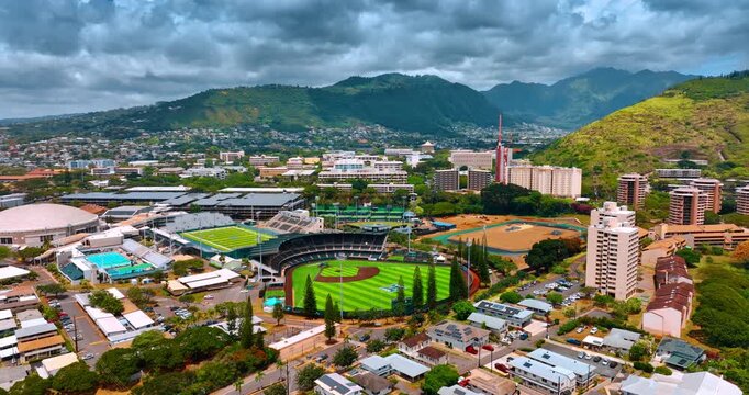 Approaching the stadiums of Hawaii University in Honolulu. Dramatic cloudscape over the verdant mountains at backdrop. Aerial perspective.