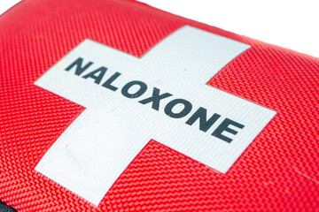 Close-up of a red naloxone pouch showing a white cross and bold black text on textured fabric.
