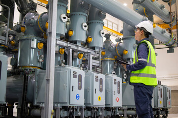 Power station staff working in industrial facility inspecting electrical equipment with safety helmet and reflective vest for maintenance and operation control