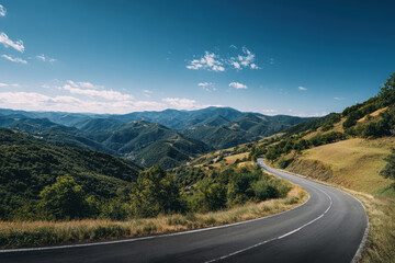 Fototapeta premium Winding mountain road through lush green hills under a vibrant blue sky on a sunny day
