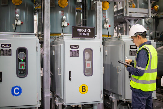 Power station staff working on electrical control panel with safety helmet and reflective vest in industrial environment - Powered by Adobe