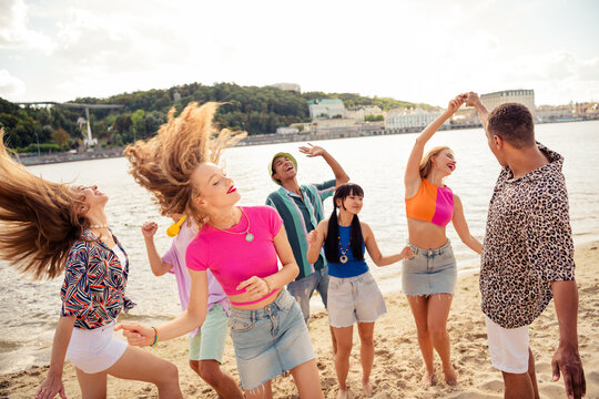Joyful young friends enjoying a summer party on a sandy beach during a sunny day by the water - Powered by Adobe