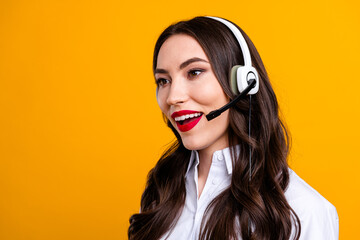 Young woman wearing a white shirt and headset looking professional against yellow background, focused and smiling brightly