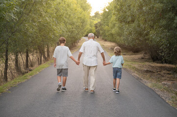 Horizontal photography with copy space of randfather with his two grandchildren walking along a...