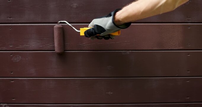 hand with paint roller painting wooden house exterior siding with protective color. wood protection
