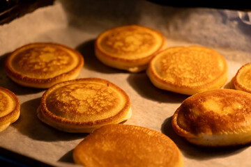 Warm golden-brown pancakes freshly baked in the oven, resting on parchment paper, offering a comforting homemade breakfast or delightful sweet dessert