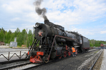 A retro steam locomotive of the mid-20th century with a smoking pipe arrives at the Ruskeala station in Karelia