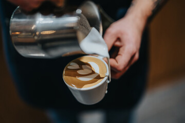 Close-up of a barista pouring milk into a coffee cup to create latte art. Focuses on the craftsmanship and creative skill required to form intricate designs in a beautifully prepared beverage.