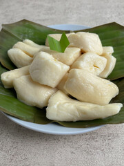 Pieces of cassava tape (tape singkong) served on green banana leaves on a white plate, a traditional Indonesian food with a soft texture and sweet flavor