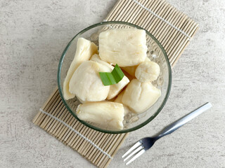 White cassava tape (singkong tape) served in a glass bowl with pandan leaf decoration, placed on a bamboo mat