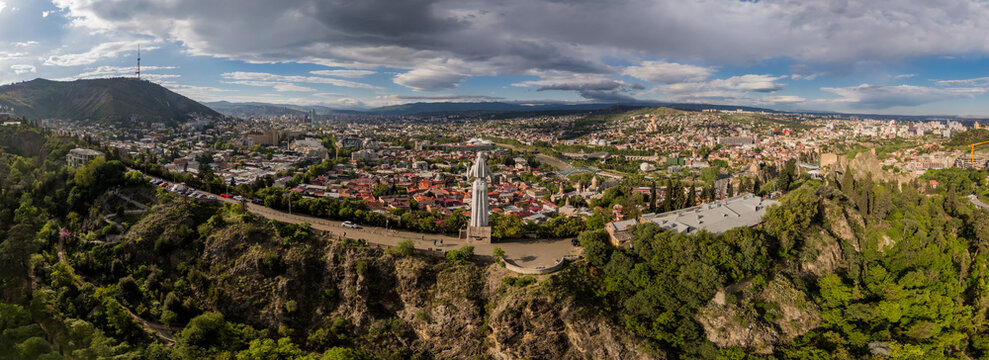 Aerial panoramic view of the Kartlis Deda statue standing majestically amidst the city's panorama, contrasting with the lush greenery and the distant mountain, Tbilisi, Georgia.