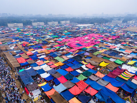 Aerial view of a sprawling tent city, a vibrant tapestry of colorful tarps, stretches out under a hazy sky, a temporary metropolis of faith and community, Dhaka, Dhaka Division, Bangladesh.