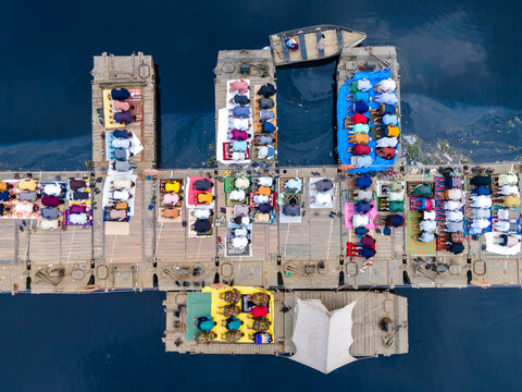 Aerial view of devotees kneeling in prayer on a floating structure, their colorful clothing a vibrant contrast against the dark water, Tongi, Dhaka Division, Bangladesh.