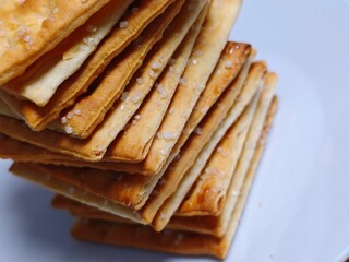 Stacked Saltine Crackers GoldenBrown Texture with Sparkling Salt Crystals on White Background.