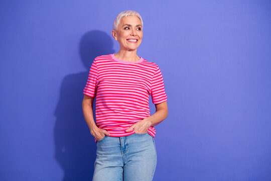 Portrait of a happy mature woman in striped t-shirt and jeans posing in front of a vibrant purple background