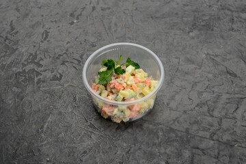 Olivier salad in disposable dishes on a gray background