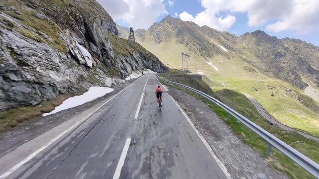Cyclist rides along a winding mountain road. Stunning scenery with rocky mountains and patches of snow. Perfect for travel, sports, and adventure themes.