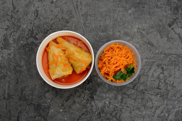 set of Ukrainian dish cabbage rolls with carrots in disposable dishes on a gray background