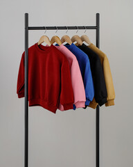 Five vibrant sweatshirts in various colors hang neatly on a simple display rack against a neutral background, showcasing a stylish selection for casual wear.
