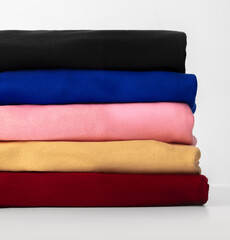 Soft textiles in vibrant shades are stacked neatly on a shelf, showcasing an array of textures. This pleasing arrangement features black, blue, pink, gold, and red fabrics.