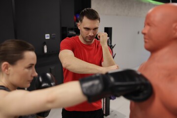 Fototapeta premium Young woman exercising with punching dummy with professional personal trainer in gym