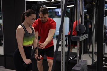 Young woman exercising with lat pulldown machine with professional personal trainer in gym