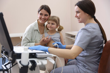Sonographer conducting little girl's abdominal ultrasound examination. Mother and daughter having appointment with doctor in clinic