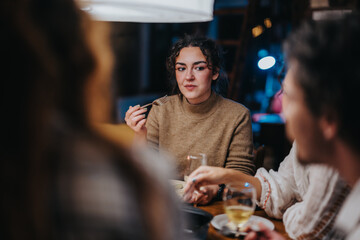 A group of friends gathered around a table, sharing a meal and conversations in a cozy indoor atmosphere. The warm lighting and relaxed setting create a comfortable and inviting mood.