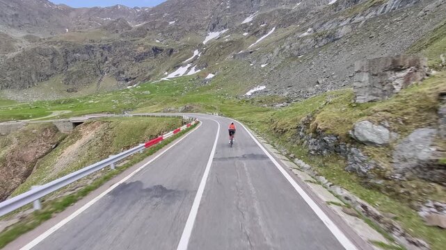 Cyclist riding a road bike on a scenic mountain pass. Stunning landscape with green hills and patches of snow. Perfect for travel, sports, or nature themes.
