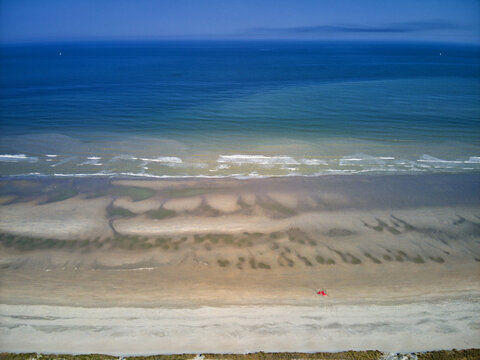Aerial view of the stark contrast between the deep blue sea and the sandy beach with intricate patterns, Dunkirk, Nord, France.