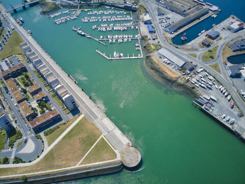 Aerial view of a vibrant harbor with boats docked amidst green waters, juxtaposed against the urban landscape of Dunkirk, Nord, France.