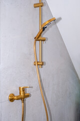 Modern gold showerhead and faucet mounted on a textured concrete wall, showcasing sleek design and contemporary bathroom aesthetics with a minimalist approach