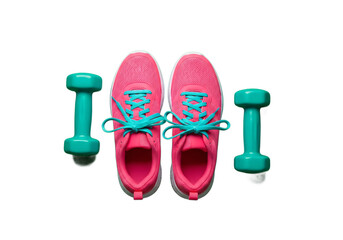 Bright pink athletic running shoes with turquoise laces and two turquoise dumbbells arranged on a black surface isolated on transparent background