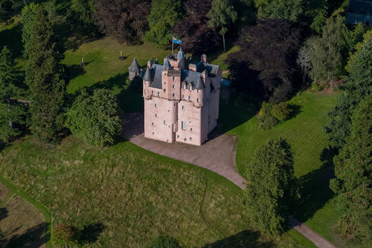 Aerial view of Craigievar Castle stands majestically amidst a sea of emerald green, its pinkish hue a stark contrast to the surrounding verdant foliage, Alford, Scotland, United Kingdom.