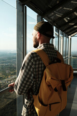 Man with yellow backpack looking through the glass at a scenic panoramic view from Avala Tower in Belgrade, Serbia