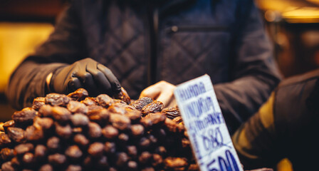 Man selecting dates at a local market stall, wearing gloves and dark jacket, with a handwritten Turkish discount sign visible, showcasing traditional shopping.