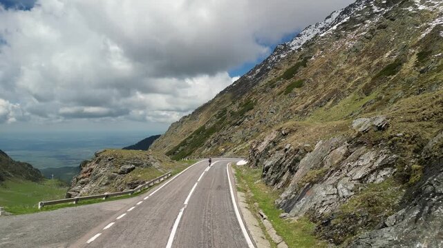 Cyclist climbs a mountain road. Stunning landscape with cloudy sky, rocky hills, and patches of green. Perfect for travel, sports, or nature projects. High-quality photo.