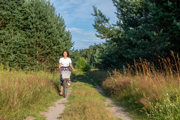 Woman riding bicycle along a scenic path surrounded by lush greenery and tall grass, enjoying nature and promoting wellness in a serene outdoor environment