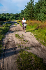 Obraz premium Woman riding bicycle along a dirt path surrounded by lush greenery, enjoying nature and the outdoors, embodying wellness and a leisurely lifestyle in a serene environment